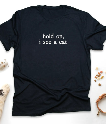 Black funny cat t-shirt with "Hold On, I See A Cat" design, flat lay top view