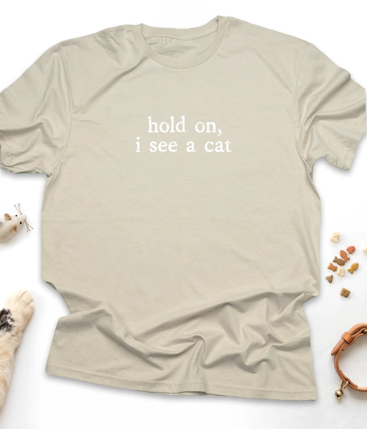 Sand funny cat t-shirt with "Hold On, I See A Cat" design, flat lay top view