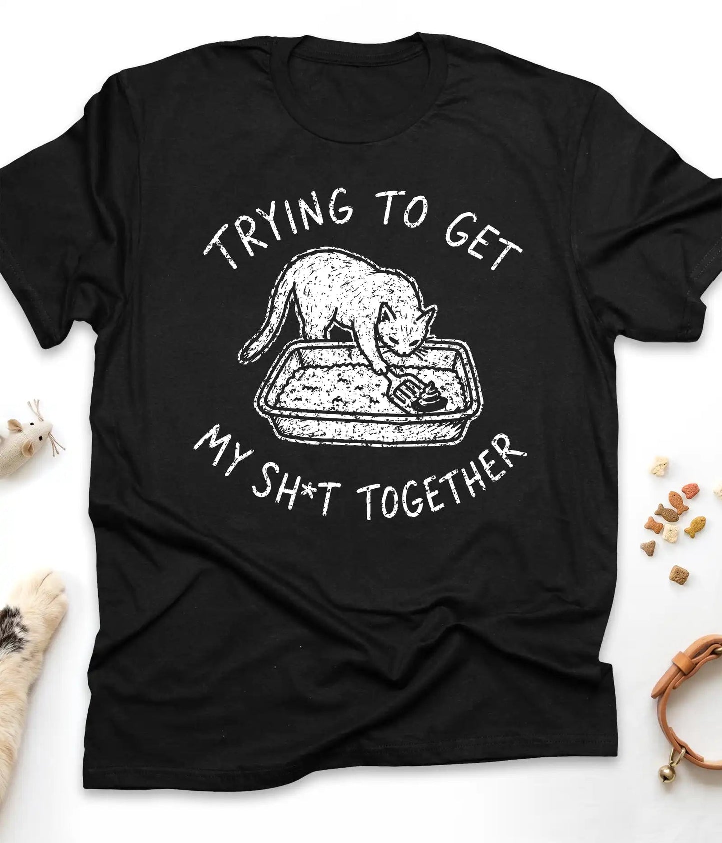 Black funny cat t-shirt with "Trying To Get My Shit Together" litter box design, flat lay top view