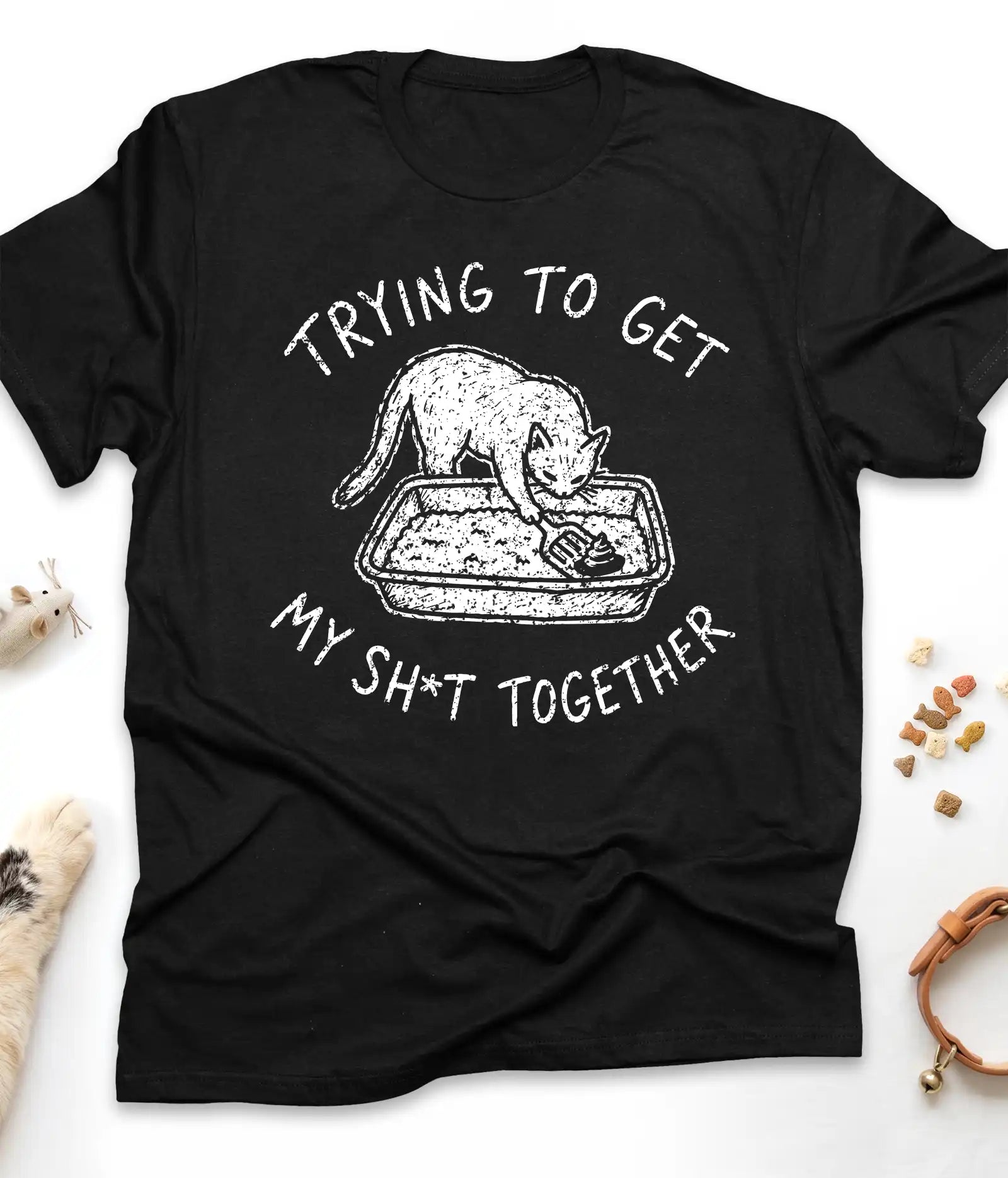 Black funny cat t-shirt with "Trying To Get My Shit Together" litter box design, flat lay top view