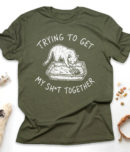 Military Green funny cat t-shirt with "Trying To Get My Shit Together" litter box design, flat lay top view