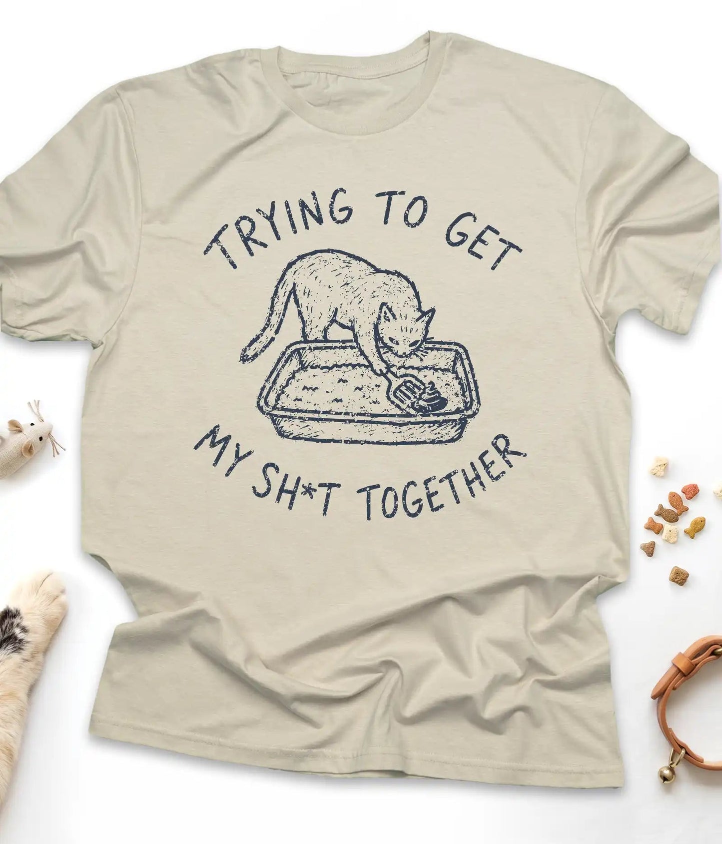 Sand funny cat t-shirt with "Trying To Get My Shit Together" litter box design, flat lay top view