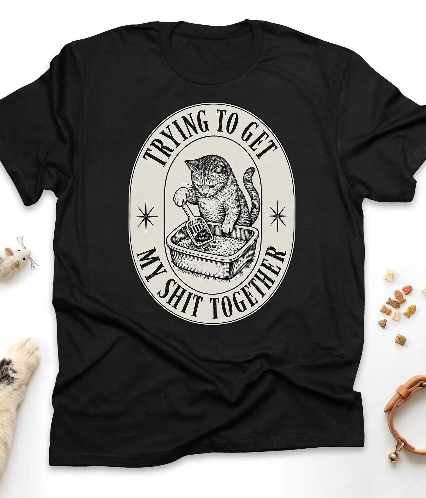 Black funny cat t-shirt with a vintage "Trying To Get My Shit Together" litter box design, flat lay top view