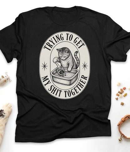 Black funny cat t-shirt with a vintage "Trying To Get My Shit Together" litter box design, flat lay top view