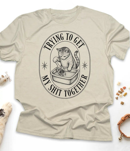 Sand funny cat t-shirt with a vintage "Trying To Get My Shit Together" litter box design, flat lay top view