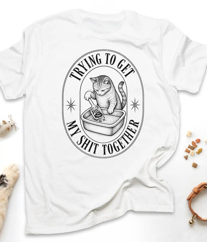 White funny cat t-shirt with a vintage "Trying To Get My Shit Together" litter box design, flat lay top view
