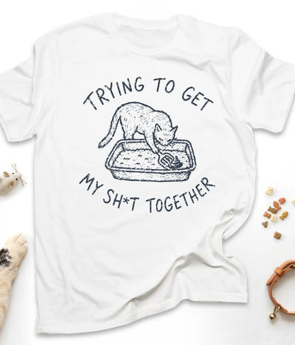 White funny cat t-shirt with "Trying To Get My Shit Together" litter box design, flat lay top view
